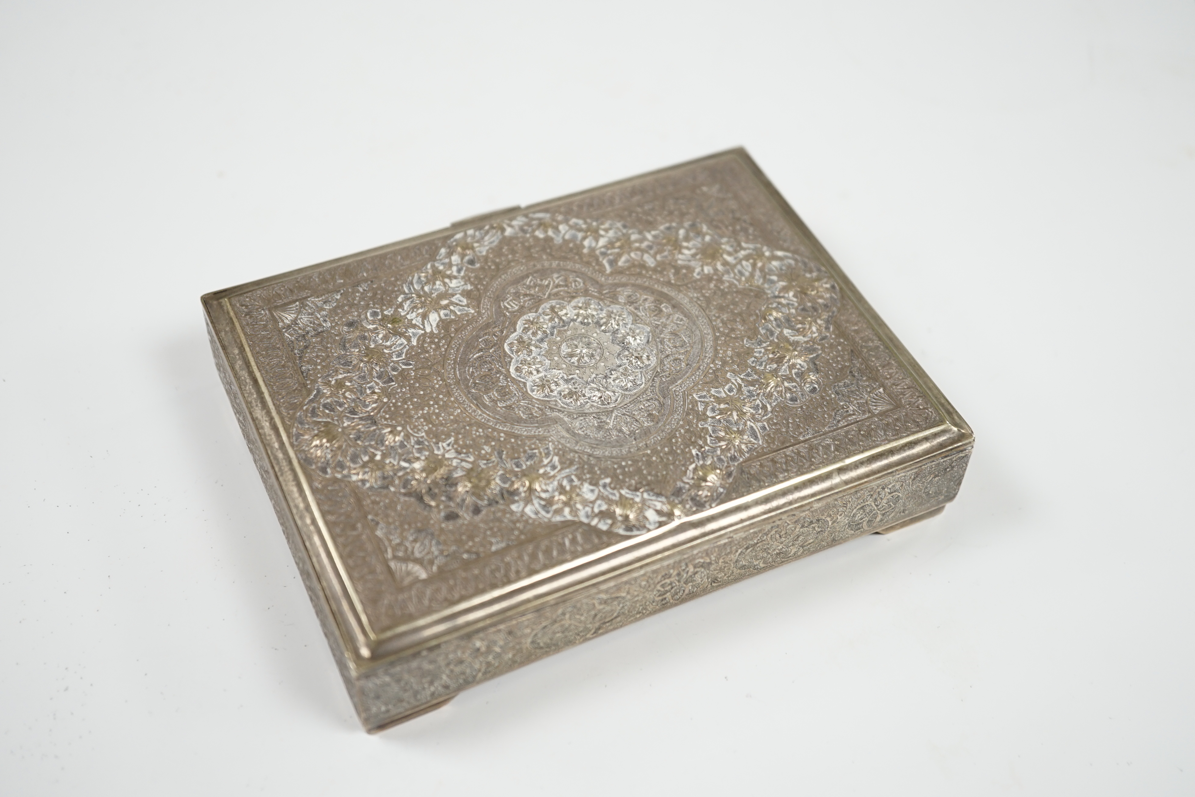 A Persian embossed white metal rectangular cigarette box, on small bracket feet, 12.2cm, 8.6oz. Condition - fair